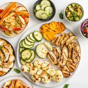 "Healthy air fryer snacks and meals including zucchini chips, apple crisps, and chicken bites on a white tray"